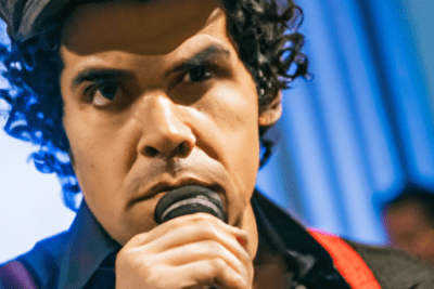 Vocalista en primer plano con micrófono interpretando 15 canciones mexicanas de critica social que no han caducado