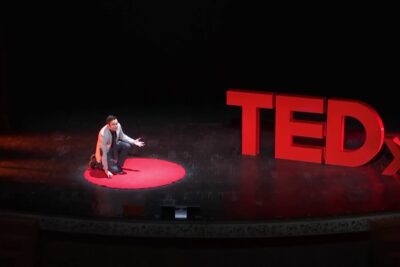 Orador arrodillado en el escenario TEDx sobre el círculo rojo AU m 7dDVR8.