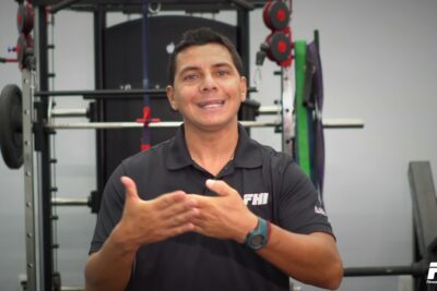 Hombre sonriente gesticulando frente a equipo de gimnasio con logo FHI L11OxYNgg4s
