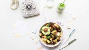 Sartén vista aérea con dados de patata dorados, champiñones salteados y medio aguacate sobre fondo blanco ajoblanco nueces thermomix receta deliciosa facil