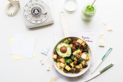 Sartén vista aérea con dados de patata dorados, champiñones salteados y medio aguacate sobre fondo blanco ajoblanco nueces thermomix receta deliciosa facil