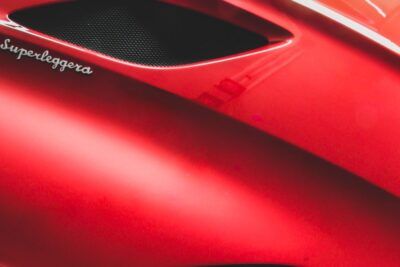 Detalle de carrocería roja brillante con emblema 'Superleggera' y rejilla, aston martin marca lider reconocida industria automotriz