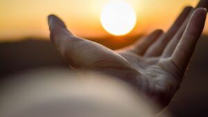 Mano abierta hacia el sol en un atardecer que aumenta conciencia espiritual anthony mello