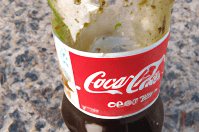 Botella plástica de Coca-Cola parcialmente vacía con líquido oscuro y residuos visibles en el interior, coca cola caducada 4 meses es seguro beberla