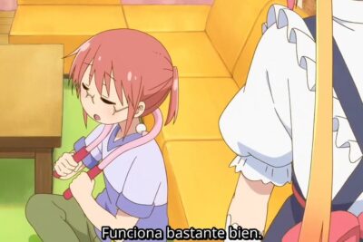 Niña de cabello rosado usando un masajeador con la cola tohru visible al fondo.