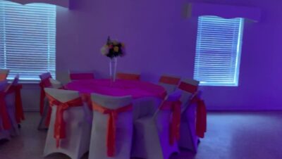 Mesa redonda con mantelería y lazos en color coral y centro floral bajo iluminación morada