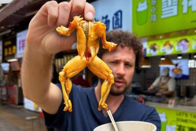 Persona sosteniendo una rana asada en un puesto callejero, imagen para comida perro