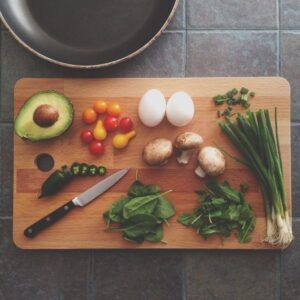 Tabla con aguacate, huevos, tomates cherry, ají picado, champiñones, cebolla china, hojas verdes y cuchillo listos para como hacer mejor receta aji gallina paso a paso delicioso