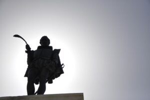 Contraluz de estatua con traje renacentista y pluma, vista desde el pedestal que sugiere una plaza histórica y como llegar alcala henares