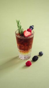 Copa alta con cóctel en capas, hielo y guarnición de frutos rojos y romero que inspira como preparar el aperol spritz perfecto para refrescar el verano.