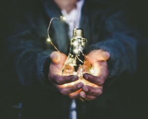 Manos sosteniendo una bombilla iluminada que simboliza consejos gestionar aire acondicionado portatil forma eficiente.