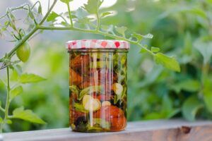 Frasco de tomates cherry conservados en aceite con dientes de ajo y hojas verdes, consejos usar ajo seco platos trucos culinarios
