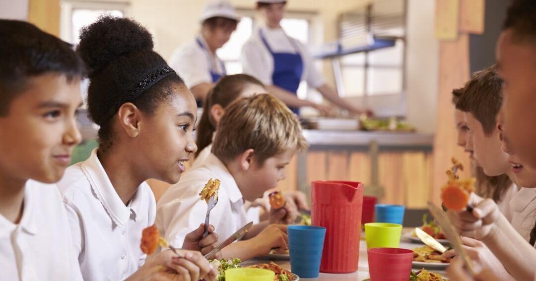 Niños comiendo en un comedor escolar mientras se plantea cual es el ingreso familiar minimo para becas de comedor.