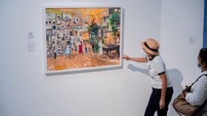 Visitantes con mascarilla observan una pintura de sala familiar que sugiere cual es el significado de echar lena al fuego