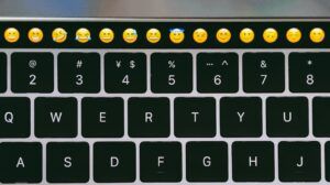 Teclado de laptop con barra táctil mostrando una fila de emojis sonrientes que invita a preguntar cual es sentido emoji.