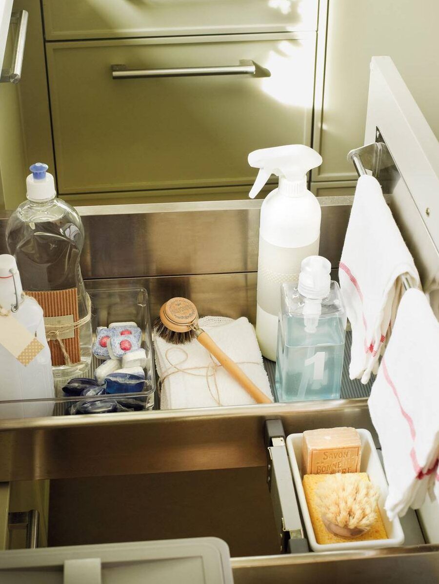 Productos de limpieza organizados en un fregadero con botellas, esponjas y cepillo, cuidado que pasa si mezclas lejia y amoniaco descubre la peligrosa reaccion quimica