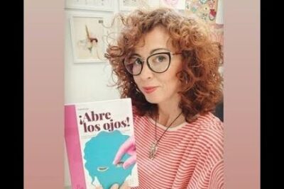 Mujer con gafas de montura oscura y cabello rizado sosteniendo un libro en un espacio interior, descubre el fascinante mundo de las gafas polarizadas que significa realmente este termino