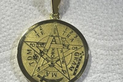 Colgante redondo dorado con pentagrama grabado y símbolos sobre fondo de tela, descubre el misterio detras del significado de 925 en un anillo.