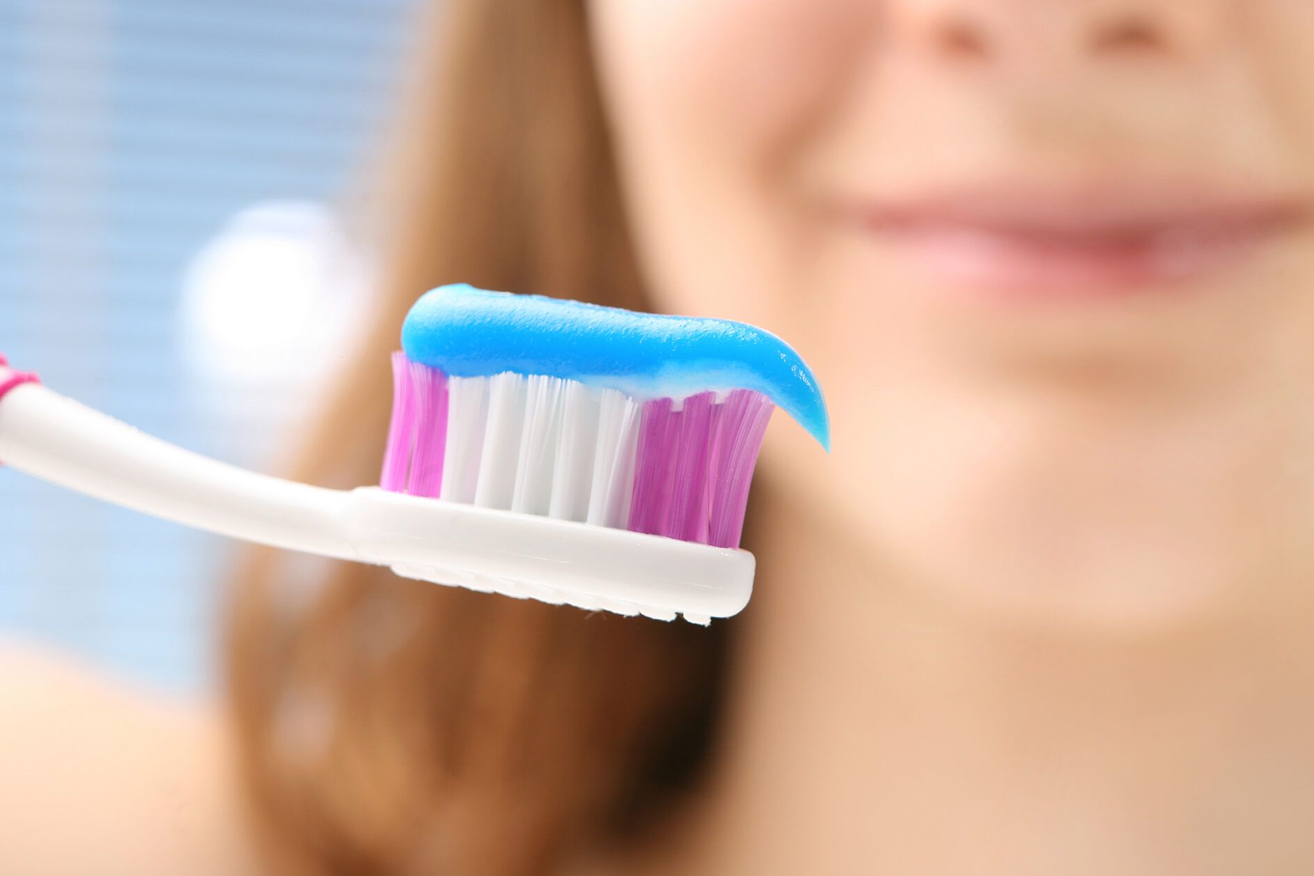 Cepillo de dientes con pasta azul en primer plano junto a una sonrisa desenfocada que sugiere descubre el secreto para una limpieza dental perfecta en las muelas con el hilo dental