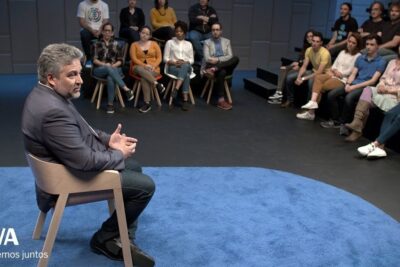 Moderador sentado en estudio hablando frente a un público en círculo, descubre el verdadero significado de 000 y su importancia en diferentes ambitos