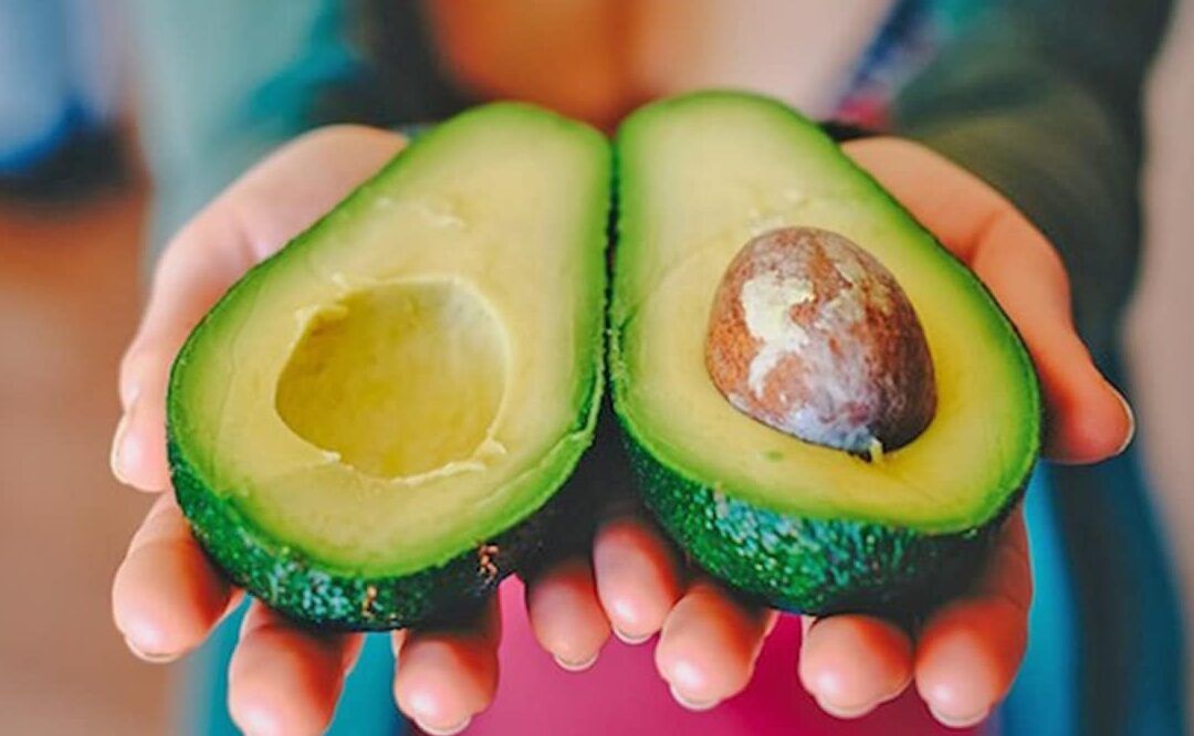 Manos que sostienen un aguacate partido mostrando la pulpa verde y el hueso, ideal para descubrir las frutas ricas en vitamina d y sus beneficios para tu salud 1