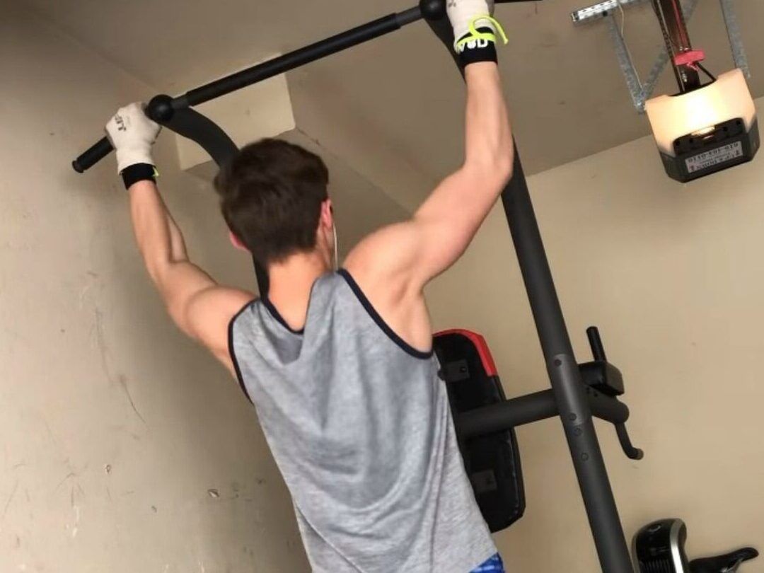 Persona de espaldas realizando dominadas en una estación de entrenamiento en casa, descubre los sorprendentes resultados de hacer 100 flexiones al dia