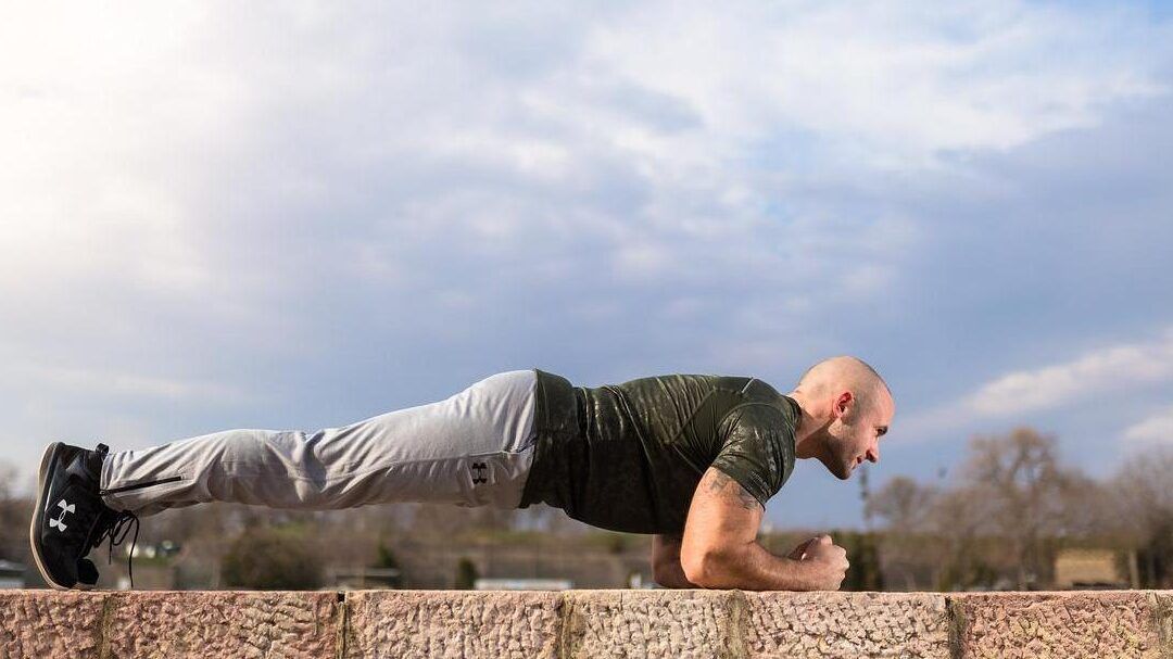 Hombre haciendo plancha al aire libre sobre un muro, descubre que le sucede a tu cuerpo si haces 1000 abdominales diarios.
