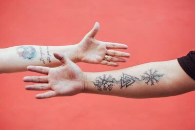 Dos antebrazos con tatuajes variados sobre fondo rojo, descubre que representa un tatuaje de media luna 1 en los motivos visibles.