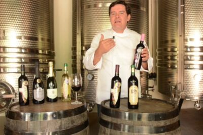 Persona en bodega presentando botellas de vino junto a tanques y barriles, descubre que se come en uruguay una deliciosa mezcla de tradicion y sabor
