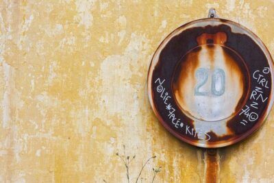 Placa oxidada con el número 20 sobre pared amarilla, descubre que simboliza el numero en la numerologia