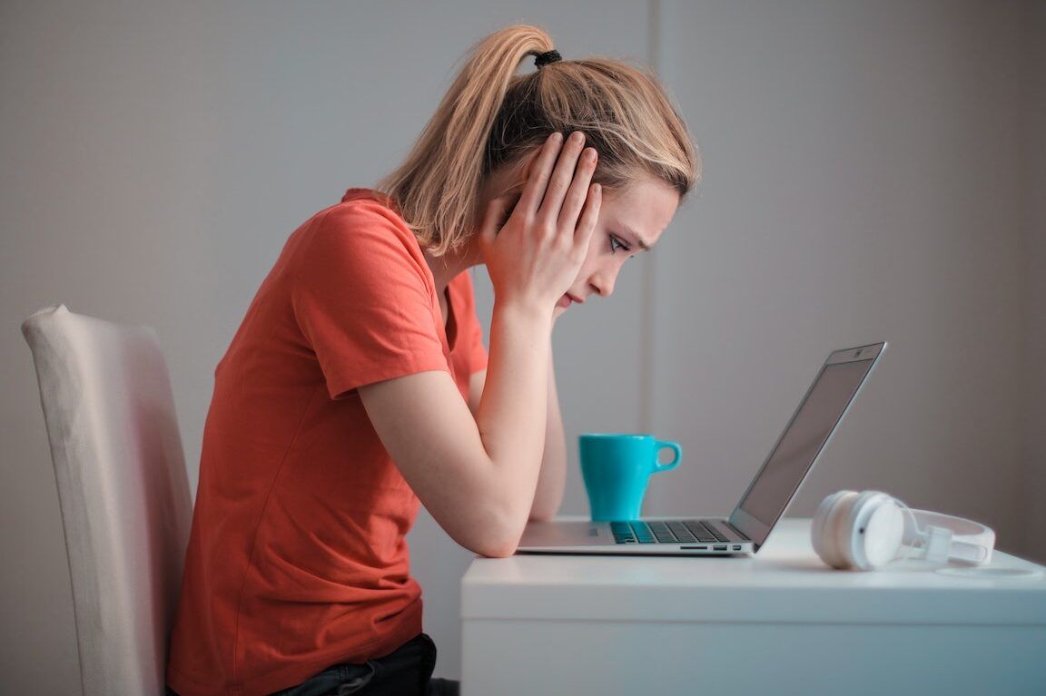 Mujer con gesto preocupado mirando un portátil junto a una taza y auriculares, descubre que sucede si estas en asnef kit digital.