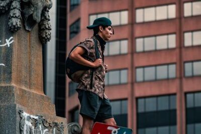 Joven de pie sobre un monumento con cartel en la ciudad que invita a descubrir significado dar clavo