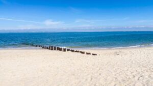 Playa de arena blanca y mar azul con postes de madera que se adentran al mar, descubre significado emoji importancia