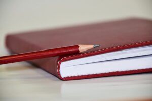 Cuaderno rojo con lápiz apoyado en tapa, descubre significado emoji todo necesitas saber