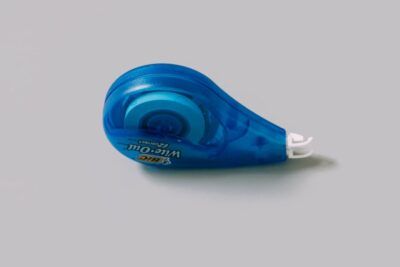 Corrector de cinta azul transparente con cabezal blanco sobre fondo gris, descubre significado meter pata evita errores