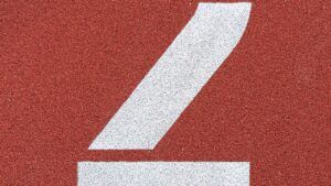Marca blanca pintada sobre pista roja texturizada que invita a descubre significado numero dos
