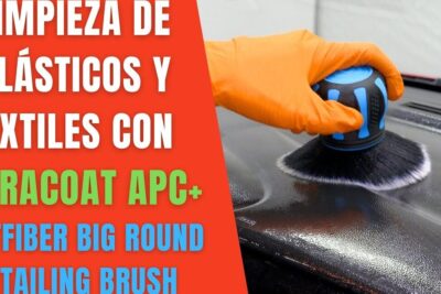 Mano con guante naranja frotando plástico con cepillo redondo y botella de limpiador visible, descubre todo sobre que significa rather de manera detallada.