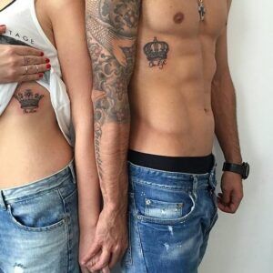 Dos personas de pie mostrando coronas a juego en el costado y el pecho, descubrir el poder y significado de un tatuaje de corona.
