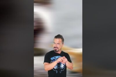 Hombre con camiseta negra gesticulando y expresando explicación sobre echas babosa frente a un fondo vertical desenfocado