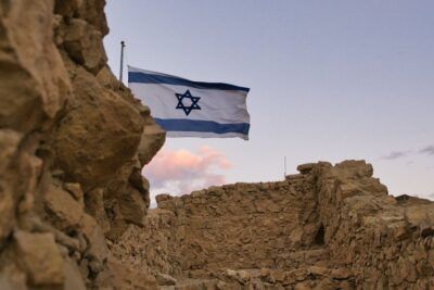 Ruinas de fortaleza en paisaje desértico con bandera israelí ondeando que evoca el asedio romano a masada