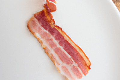 Tira de bacon cocida en un plato blanco que ilustra el peligro de consumir bacon caducado que riesgos conlleva