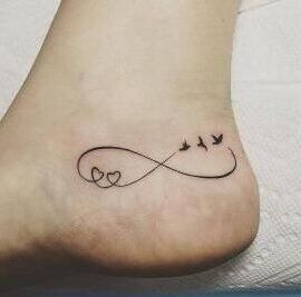 Tatuaje minimalista en el tobillo con símbolo de infinito, dos corazones en un lazo y tres aves en vuelo que representa el significado de un tatuaje de infinito en el tobillo.