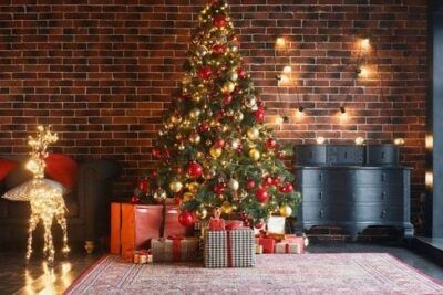 Árbol de Navidad decorado con luces, bolas y regalos junto a una figura luminosa y pared de ladrillo, el significado del arbol de la vida guia completa 1.