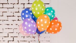 Ramo de globos de colores con lunares frente a una pared blanca, el significado del emoji descubre su sentido y significado