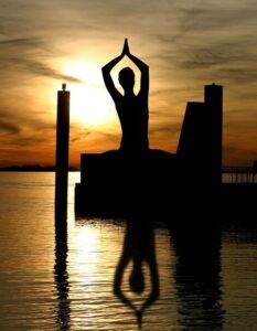 Persona en posición de meditación al atardecer con reflejo en el agua que evoca el significado del simbolo del yin y yang descubre su origen