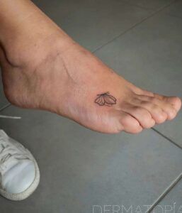 Tatuaje pequeño y lineal de mariposa en el empeine que ilustra el significado del tatuaje de mariposa en el pie 1.