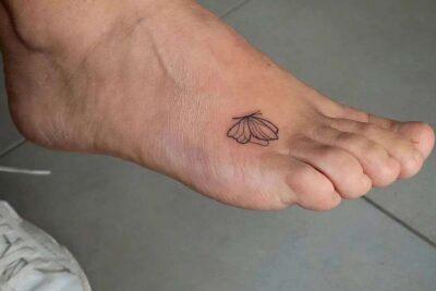 Tatuaje pequeño y lineal de mariposa en el empeine que ilustra el significado del tatuaje de mariposa en el pie 1.