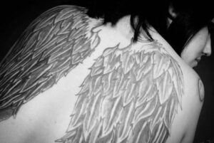 Vista posterior de una persona con un tatuaje grande de alas en la espalda, referencia para el simbolismo de un tatuaje de angel en la muneca significado y mas 1.