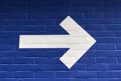 Flecha blanca pintada hacia la derecha sobre pared de ladrillo azul que evoca el simbolismo y significado tatuaje flecha arriba.