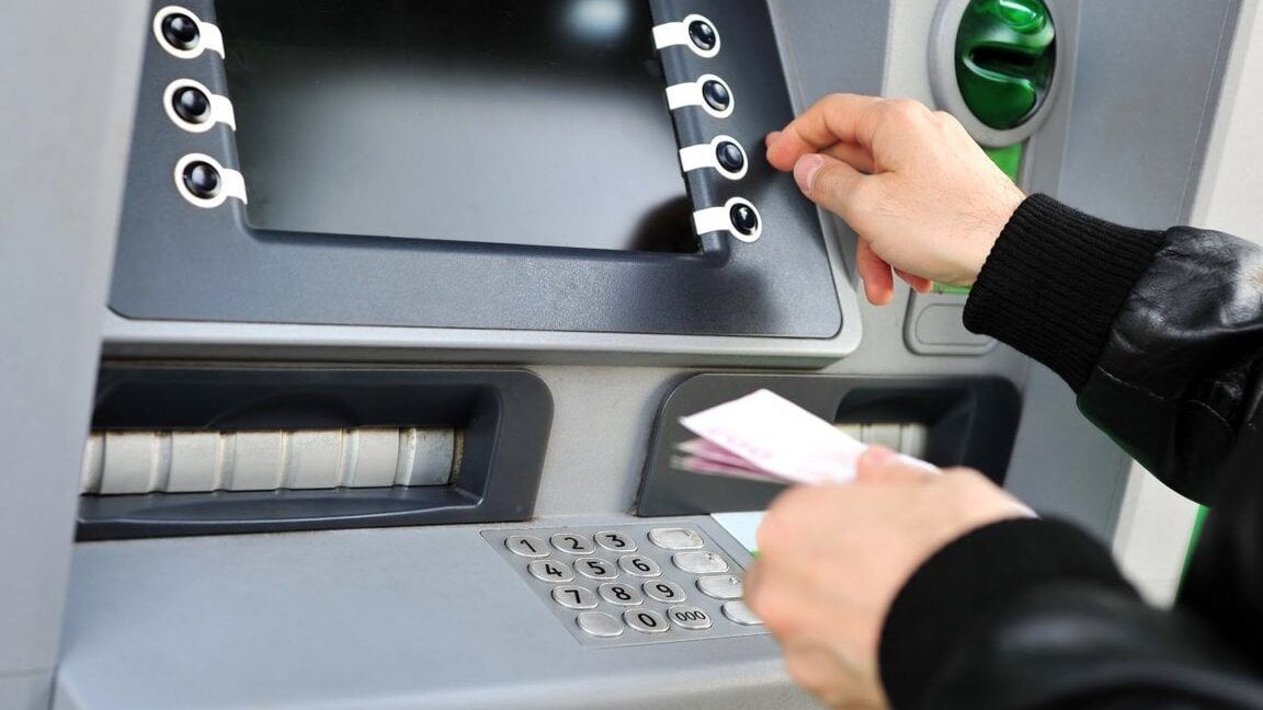 Persona usando un cajero automático con teclado numérico y billetes en la mano, es legal ingresar grandes cantidades de dinero en zelle descubre aqui